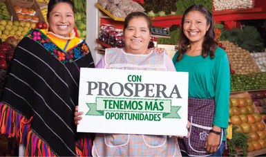Tres mujeres en un mercado de fruta sostienen un letrero que dice "Con Prospera tenemos más oportunidades"