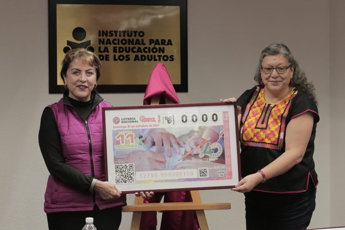 Fotografía de Margarita González Saravia Calderón y Teresa Guadalupe Reyes Sahagún sosteniendo la ampliación del billete develado alusivo a los 40 años del INEA