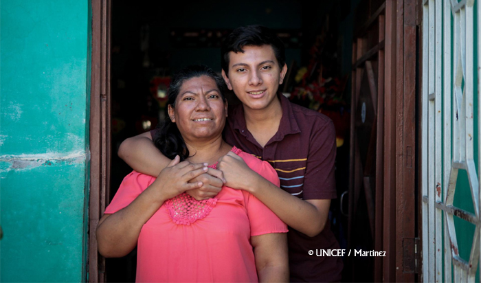 Madre y su hijo adolescente en la puerta de su casa, abrazados y sonrientes. Foto:  © UNICEF / Martínez