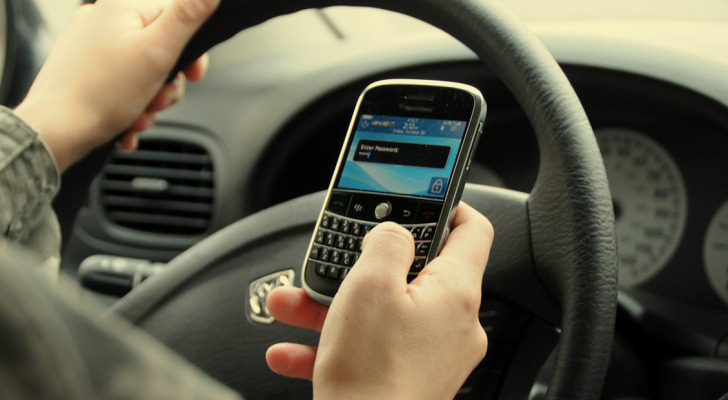Unas manos en el volante de un auto y va enviando mensajes de texto mientras conduce.