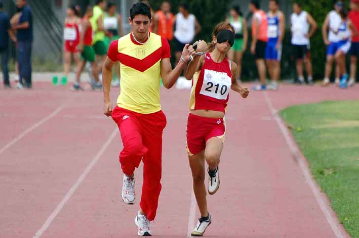 Atleta con discapacidad visual corre al lado de su guía en competencia de atletismo.