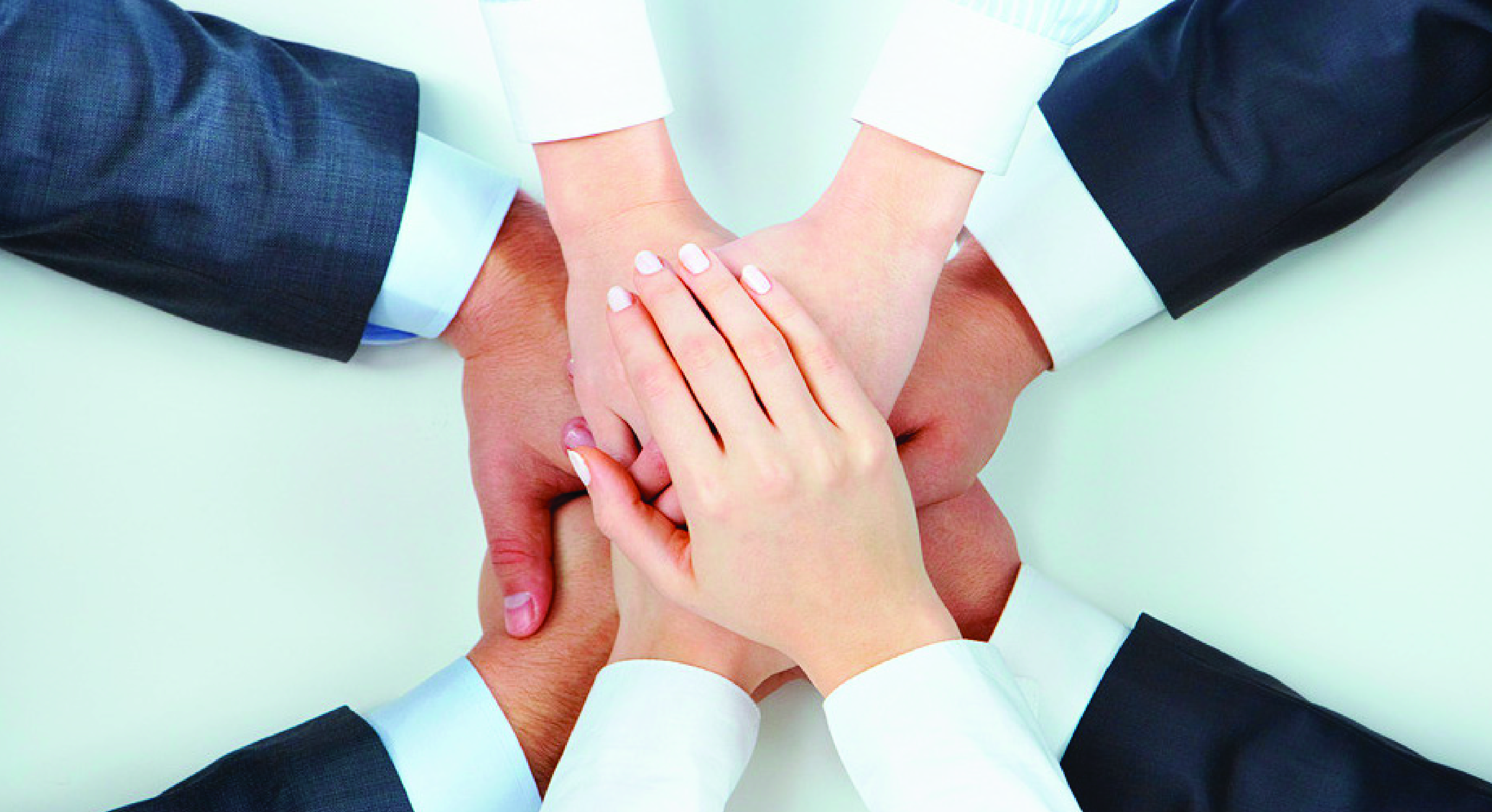 Varios hombres y mujeres unen las manos en señal de que trabajan en equipo.