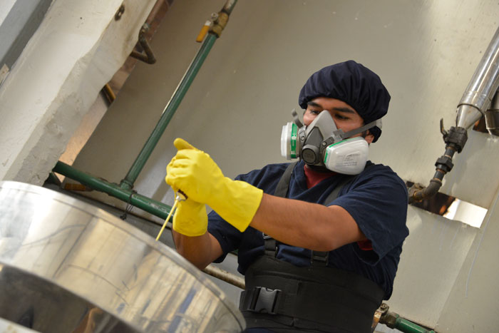 Hombre bien equipado con mascarilla, guantes y cofia, trabajando con químicos.