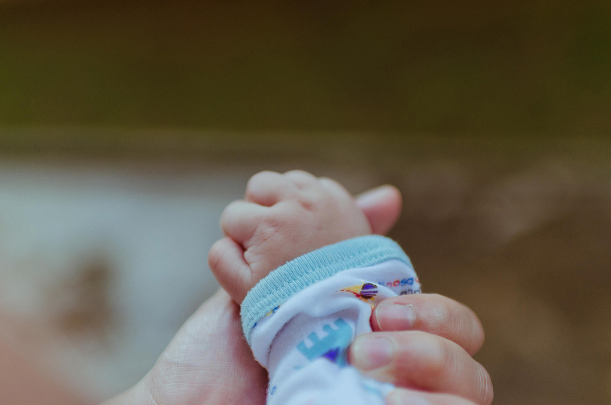 Fotografía de una mano de una persona adulta sosteniendo una mano de un bebé