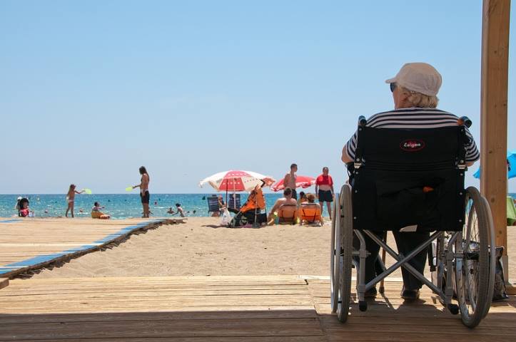 Mujer con discapacidad usuaria de silla de ruedas disfrutando de la playa accesible.