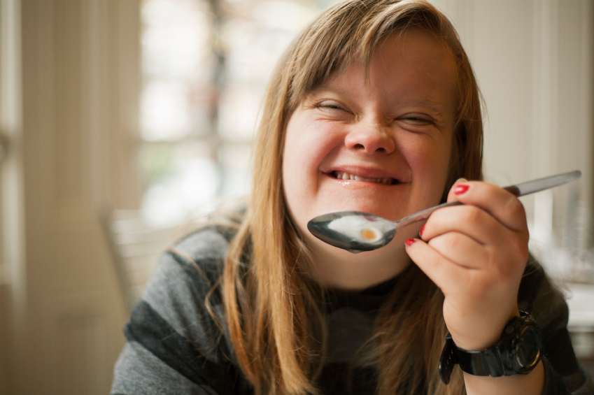 Chica con Síndrome de Down sonríe mientras sostiene una cuchara con comida