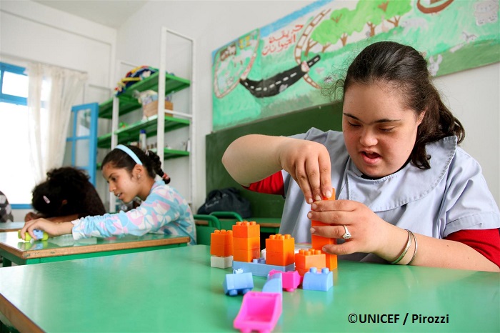 Chica adolescente con síndrome de Down, en salón de clases, usa piezas Lego de juego.