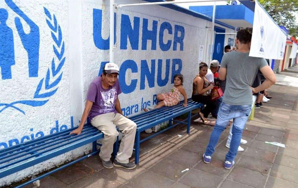 Personas sentadas en banca afuera de oficinas de ACNUR