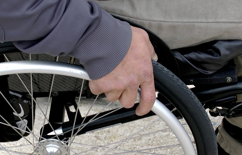 Imagen cortada  de una persona en silla de ruedas, parte del brazo pierna y llanta