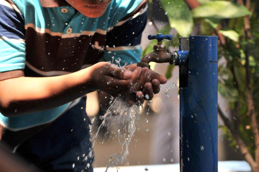 Vista general de joven utilizando sus manos para tomar agua de una toma.