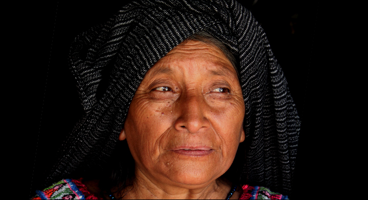 Mujer indígena con rebozo sobre su cabeza, mira serena hacia el horizonte.

