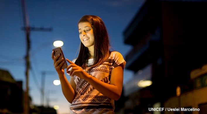Chica adolescente con teléfono en las manos, que usa para comunicarse con sus amigas y amigos.