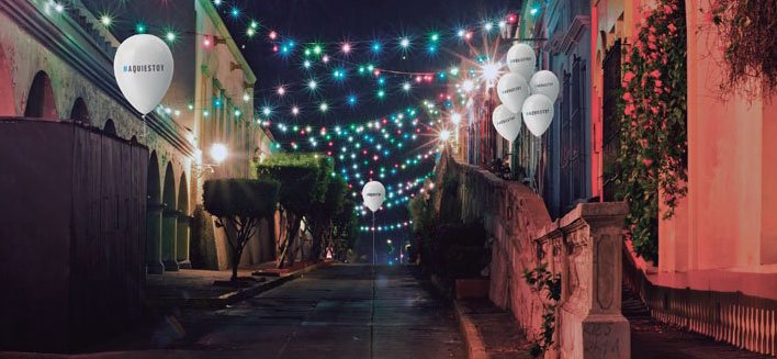 Imagen de una calle de noche adornada con cadenas de luces y globos blancos