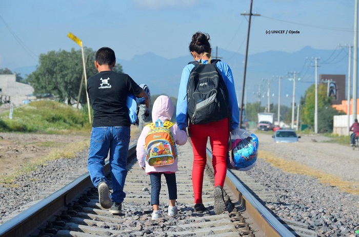Niña, niño y su madre caminan por la vía del tren.