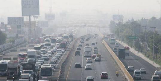 Plano general de avenida de la Ciudad de México donde se ven decenas de autos circulando por ella. Se destaca la nula visibilidad del horizonte debido a la contaminación generada por los vehículos.