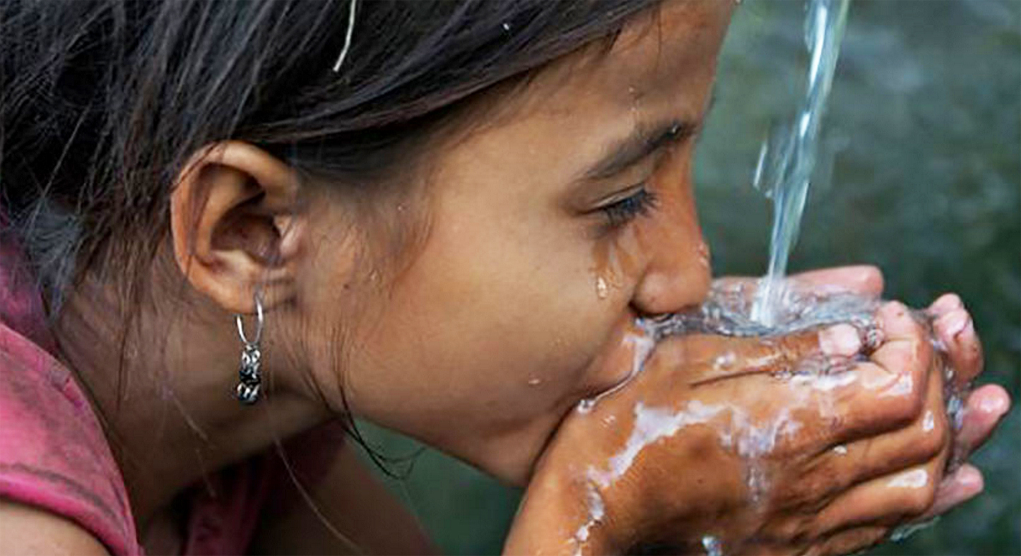 Vista lateral de niña tomado agua con sus manos.