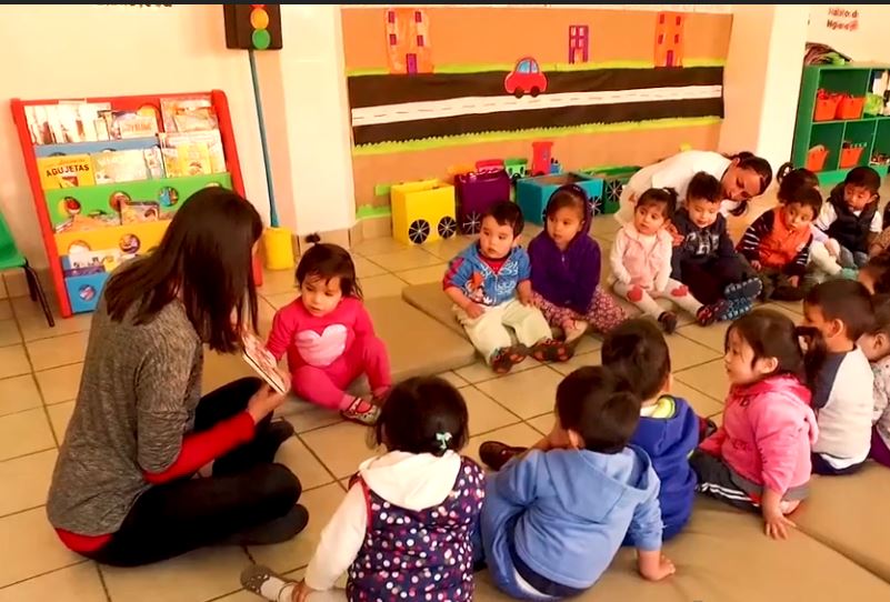 Salón de Guardería del IMSS donde niñas y niños menores a 5 años de edad escuchan atentos la lectura de un cuento.