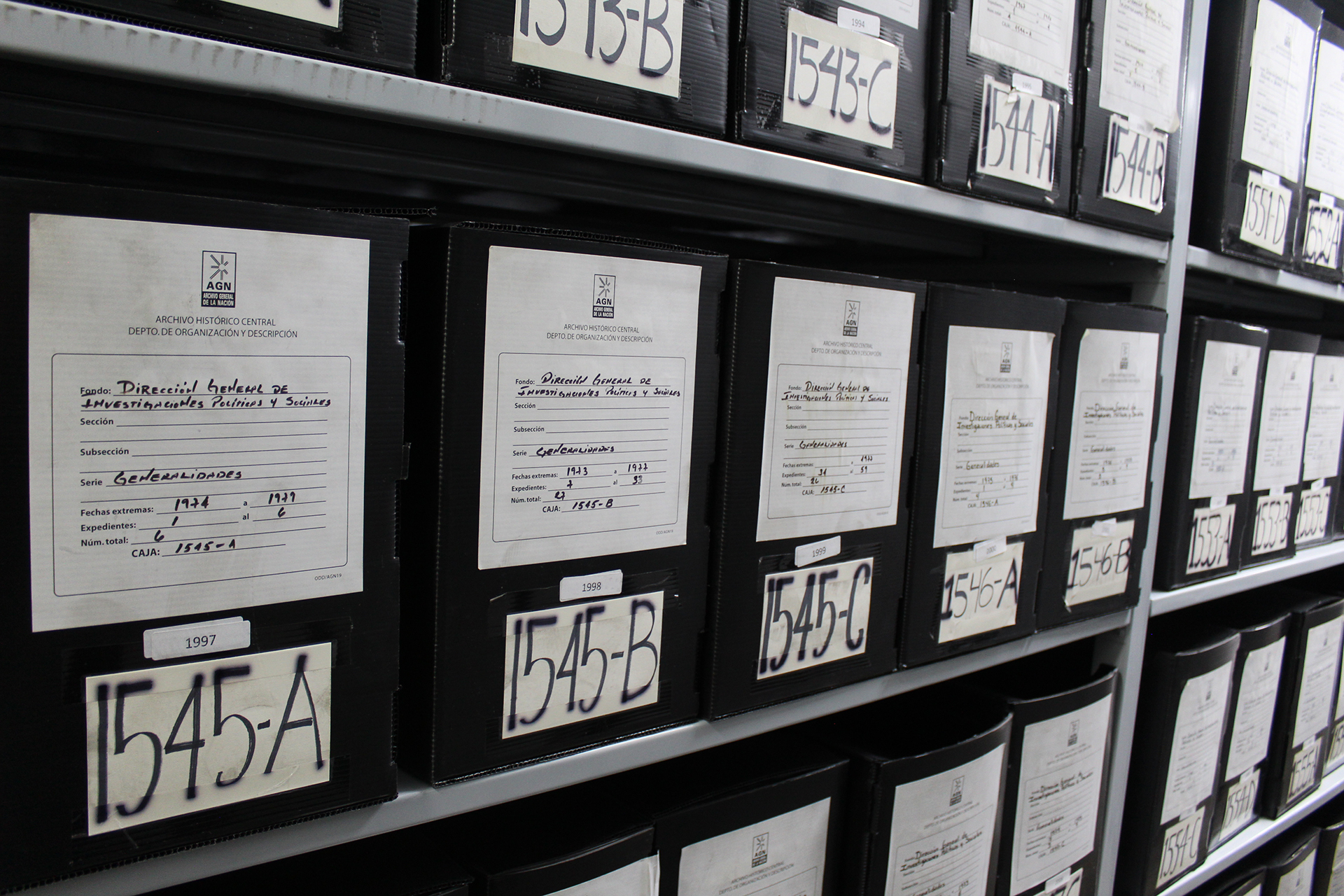 Imagen con cajas de polipropileno colocadas en estanterías, con números consecutivos y etiquetas que los identifican como fondos de la Dirección General de Investigaciones Políticas y Sociales