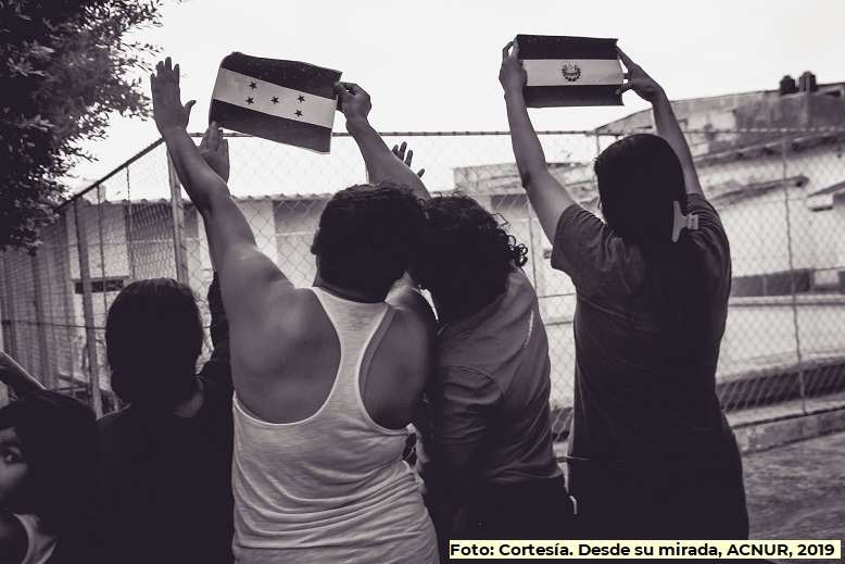Mujeres migrantes levantando las manos y mostrando las banderas de sus países