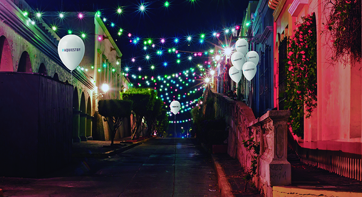 2. Paisaje urbano nocturno con globos con la leyenda #AquíEstoy.
