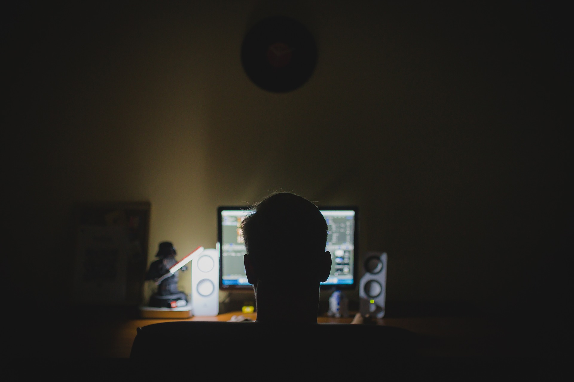 uan computadora encendida en la oscuridad remarca la silueta de un joven viendo la computadora