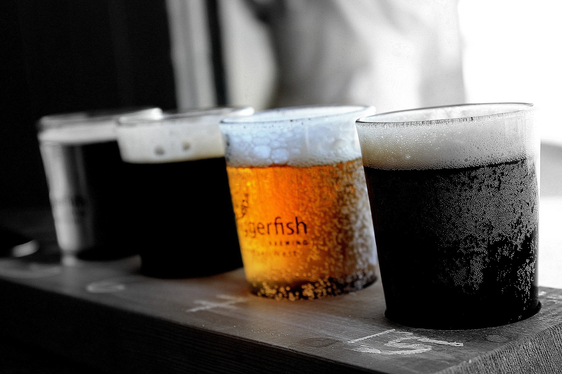 cuatro vasos de cerveza en fila tres oscuros y uno claro