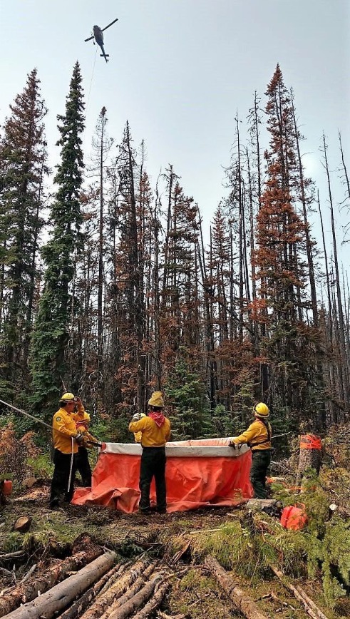 General de grupo de combatientes de incendios forestales llenando contenedor de agua, al fondo se ven pinos.