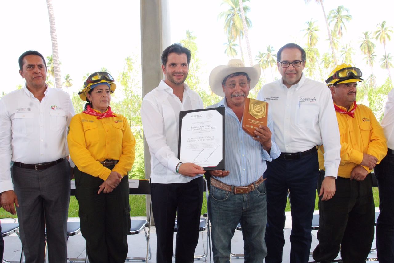 Retrato de galardonado con el Premio Nacional al Mérito Forestal 2018, mostrando su presa y reconocimiento en medio del Gobernador de Colima, José Ignacio Peralta Sánchez y el Secretario de Medio Ambiente y Recursos Naturales, Rafael Pacchiano Alamán.