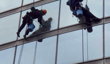 Dos hombres limpiando unas ventanas en altura