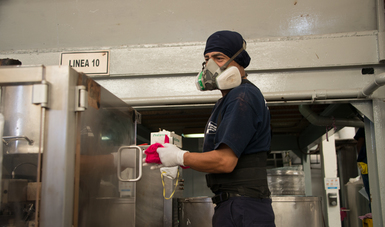 Un trabajador porta el equipo adecuado para el desempeño de sus funciones, guantes, máscara y cofia