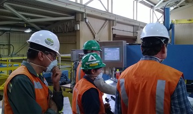 Un grupo de trabajadores equipados con chalecos y tapabocas industriales supervisan un proceso en una fábrica