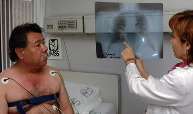 Hombre en camilla del IMSS recibe interpretación de una radiografía que le muestra doctora del Instituto.