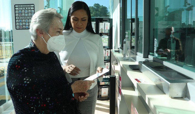 secretaria de Bienestar, Ariadna Montiel ayudando a abrir un sobre a una adulta mayor en una sucursal del Banco del Bienestar