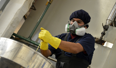 Hombre trabajando, equipado con utensilios de protección adecuados, colocando en un recipiente un tubo de pintura.