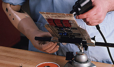 Persona con brazo mecánico trabajando en electrónica.