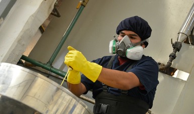 Hombre trabajando con químicos, porta cofia en el cabello, mascarilla y guantes.
