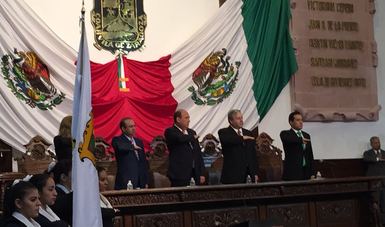 Cinco personas de pie realizando saludo a la bandera nacional.