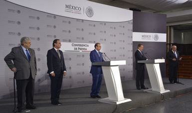 Cinco personas de pie en un estrado, viendo al frente durante una conferencia de prensa.